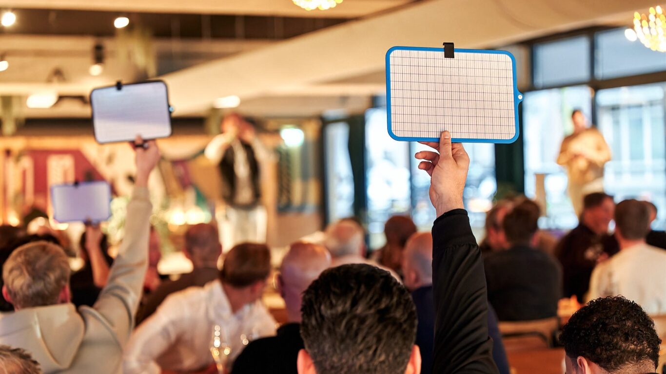 Steken scoreborden omhoog tijdens een interactieve quiz of spelavond in een volle zaal.