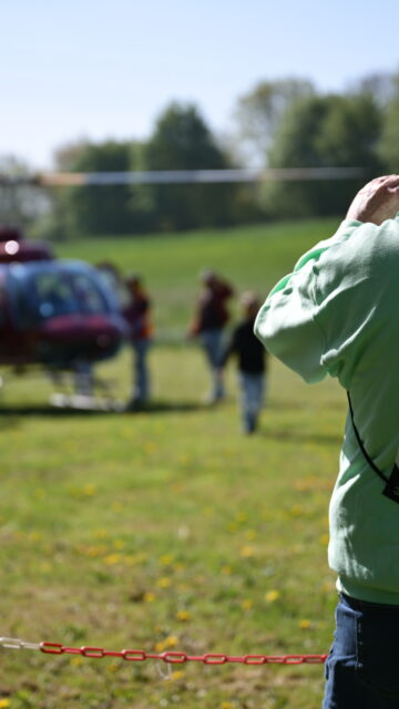 Vrijwilliger fotografeert een helikopteractiviteit tijdens een buitenevent voor kinderen op een zonnig grasveld.