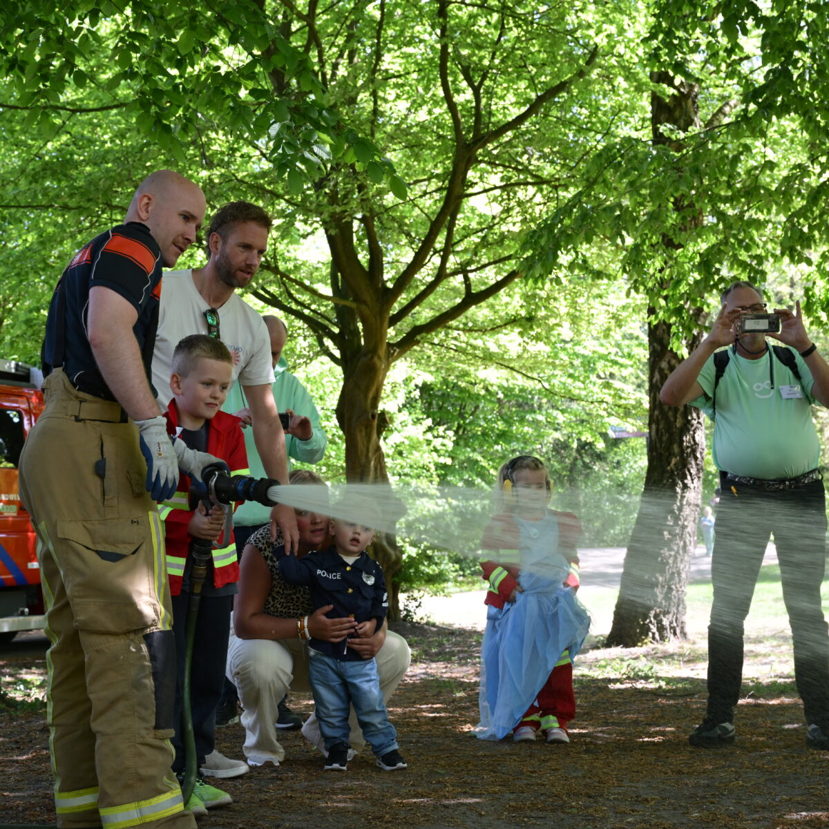 Brandweerman helpt kinderen met een brandslang tijdens een interactieve buitenactiviteit in het bos.