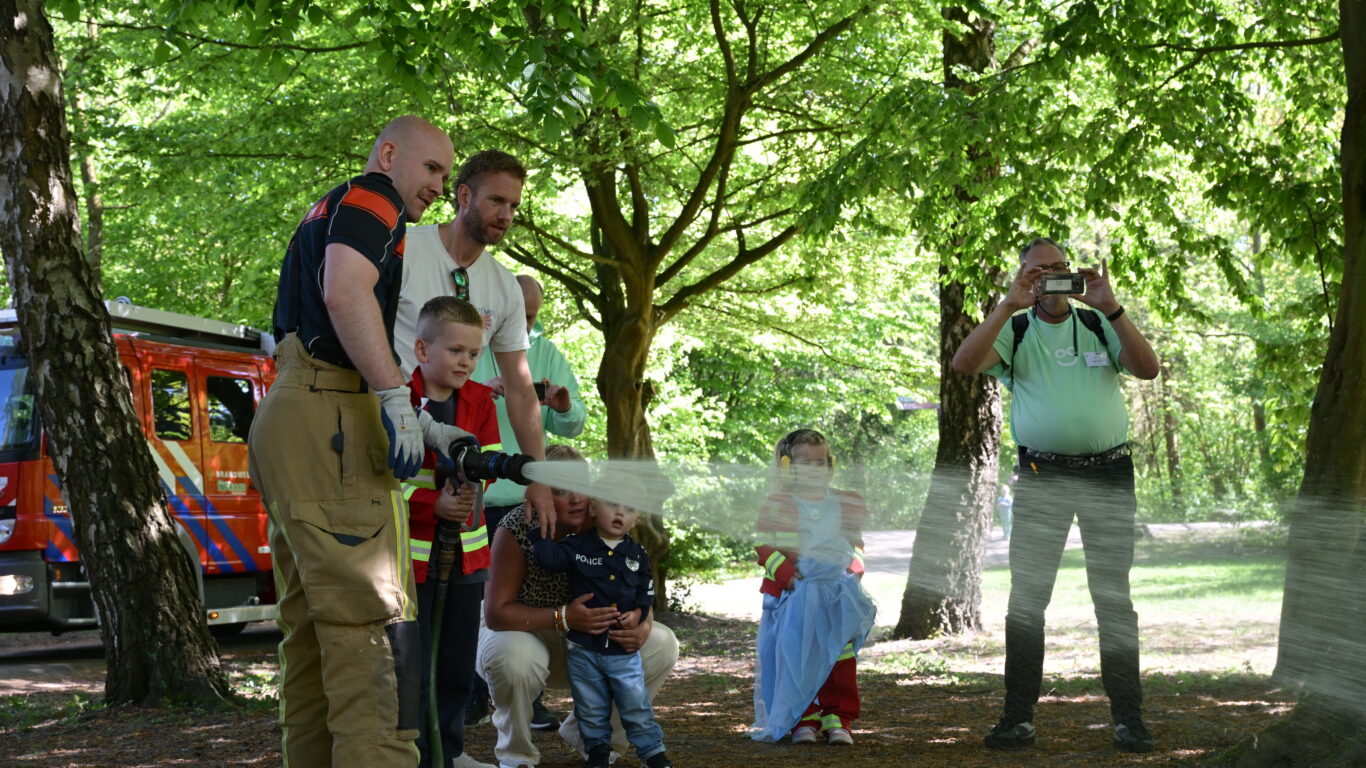 Brandweerman helpt kinderen met een brandslang tijdens een interactieve buitenactiviteit in het bos.