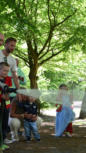 Brandweerman helpt kinderen met een brandslang tijdens een interactieve buitenactiviteit in het bos.